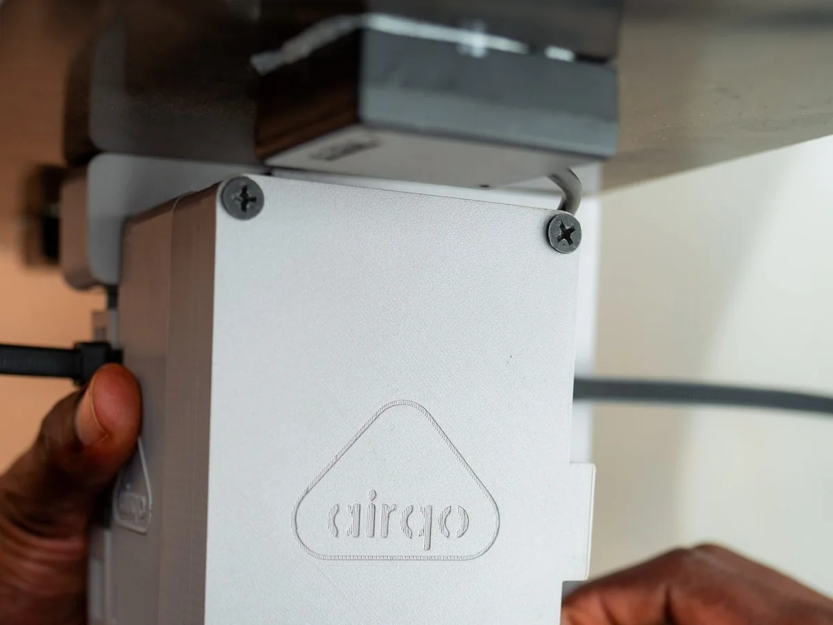 Hands mounting an AirQo air quality monitor, its case embossed with the AirQo logo
